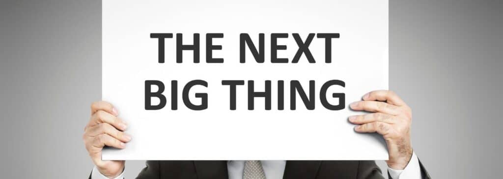 Person in a suit holds a white sign covering their face, which reads 'THE NEXT BIG THING'.