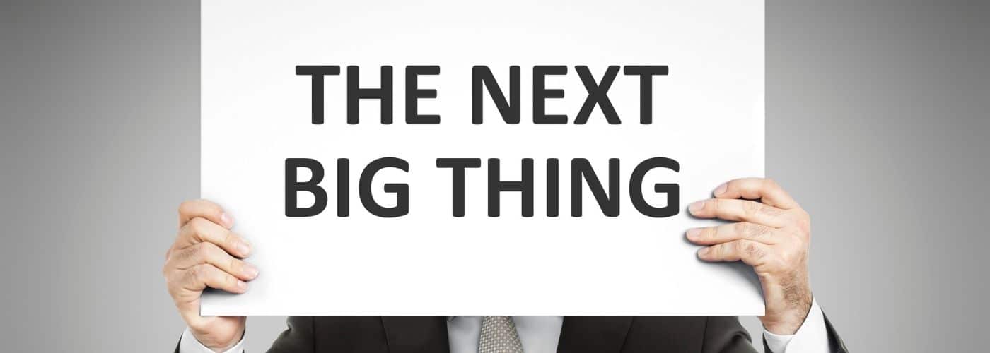 Person in a suit holds a white sign covering their face, which reads 'THE NEXT BIG THING'.