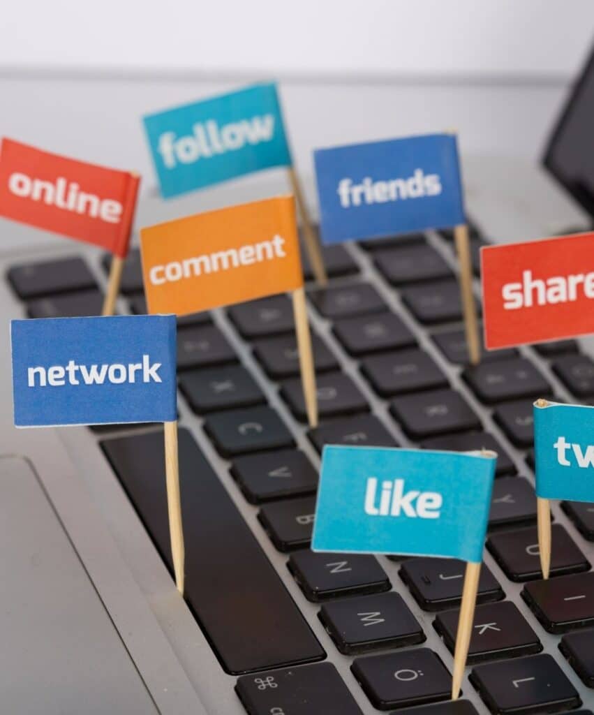 Colorful signs with social actions (like, share, comment, follow, friends, network) placed on a laptop keyboard.